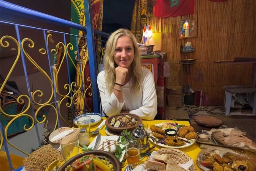 Blonde female tourist smiling at a table full of traditional food during dinner in Marrakech.